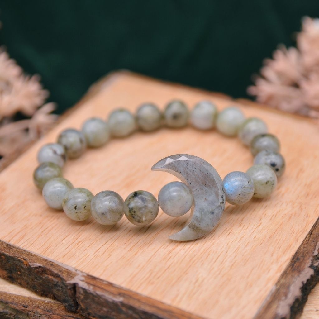 A labradorite gemstone bracelet with a crystal crescent moon and labradorite beads displayed on a wooden background.